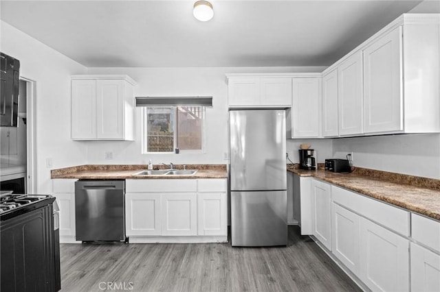 kitchen featuring appliances with stainless steel finishes, light wood-type flooring, white cabinetry, and sink