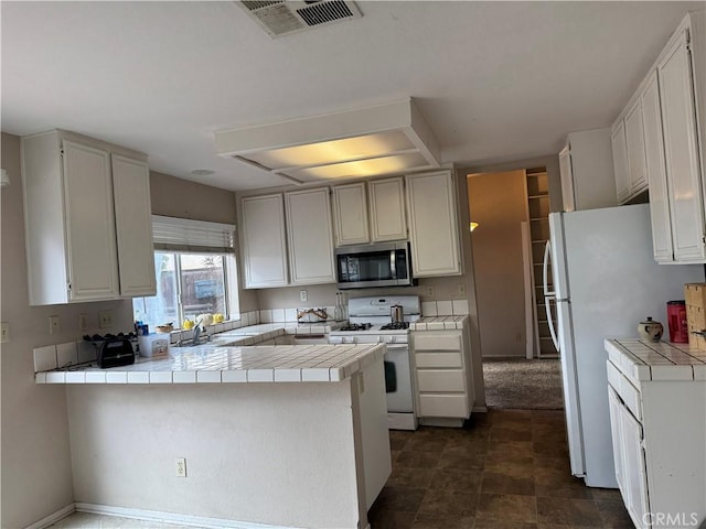 kitchen with tile countertops, sink, white cabinets, kitchen peninsula, and white appliances