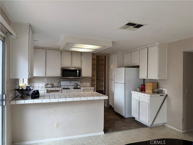 kitchen with white appliances, tile countertops, kitchen peninsula, and white cabinets