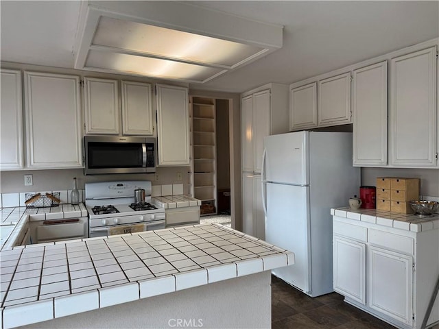 kitchen with sink, white appliances, tile counters, white cabinets, and kitchen peninsula