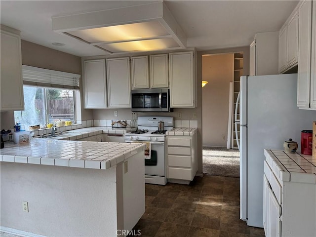 kitchen featuring sink, tile counters, kitchen peninsula, white appliances, and white cabinets