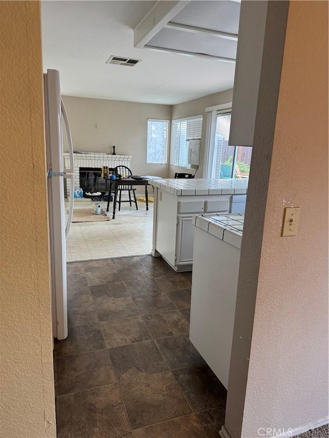 kitchen featuring white cabinetry, white refrigerator, a fireplace, tile countertops, and kitchen peninsula