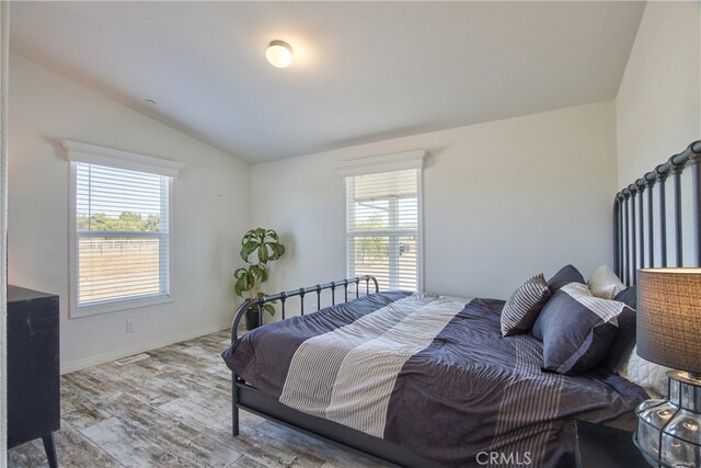 bedroom with light wood-type flooring, vaulted ceiling, and multiple windows