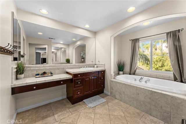 bathroom with tile patterned flooring, vanity, tiled bath, and backsplash