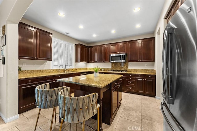 kitchen featuring sink, light stone countertops, appliances with stainless steel finishes, a kitchen island, and a breakfast bar area