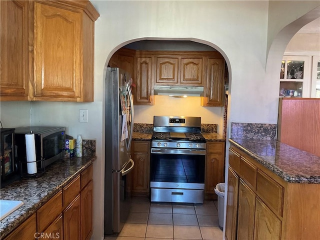 kitchen featuring light tile patterned floors, dark stone counters, and appliances with stainless steel finishes