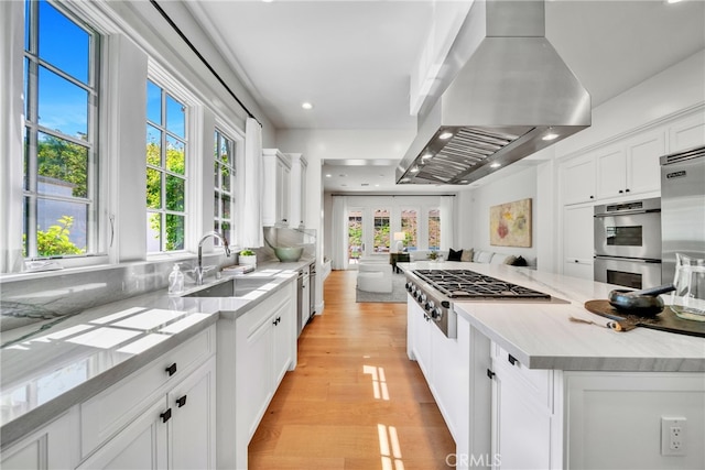 kitchen with island exhaust hood, light hardwood / wood-style flooring, sink, white cabinetry, and appliances with stainless steel finishes