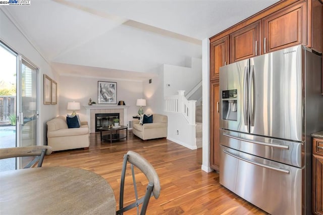 kitchen featuring stainless steel fridge, light hardwood / wood-style floors, lofted ceiling, and a tiled fireplace