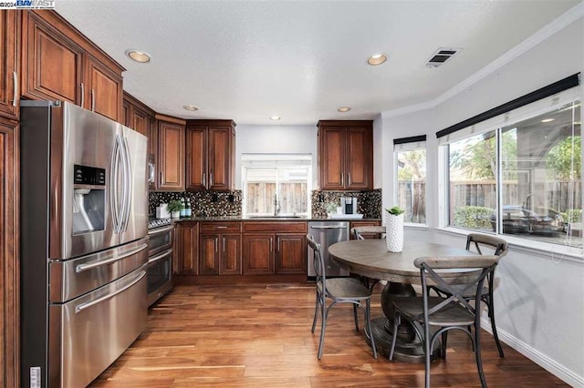 kitchen featuring appliances with stainless steel finishes, tasteful backsplash, crown molding, sink, and light hardwood / wood-style floors