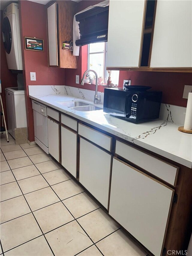 kitchen featuring white cabinetry, sink, white dishwasher, light tile patterned floors, and stacked washer and clothes dryer