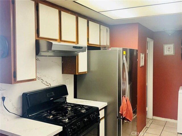 kitchen featuring black gas range, white cabinets, stainless steel fridge, light tile patterned floors, and washer / dryer