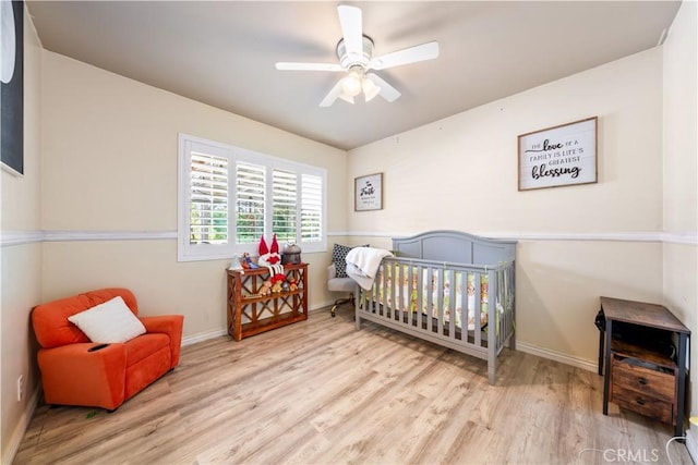 bedroom featuring light wood-type flooring, a nursery area, and ceiling fan