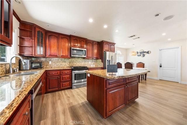 kitchen with tasteful backsplash, light stone counters, light hardwood / wood-style flooring, and stainless steel appliances