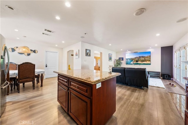 kitchen featuring stainless steel refrigerator, light stone countertops, a center island, hanging light fixtures, and light hardwood / wood-style flooring