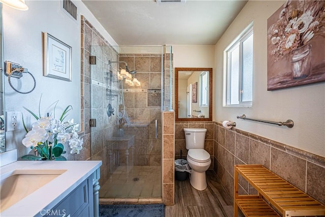 bathroom featuring wood-type flooring, an enclosed shower, toilet, vanity, and tile walls