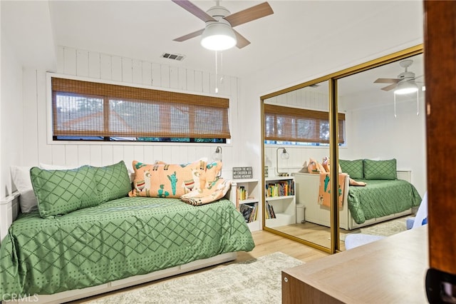 bedroom featuring a closet, ceiling fan, wood walls, and light hardwood / wood-style floors