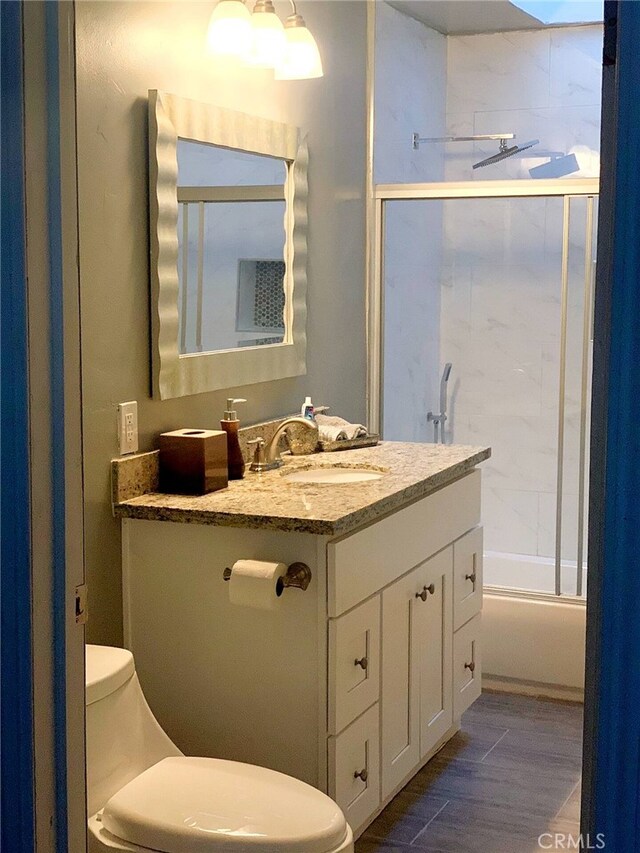 full bathroom featuring hardwood / wood-style floors, vanity, toilet, and bath / shower combo with glass door