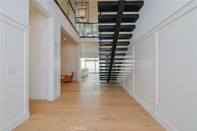 hallway with a towering ceiling, light hardwood / wood-style flooring, and an inviting chandelier