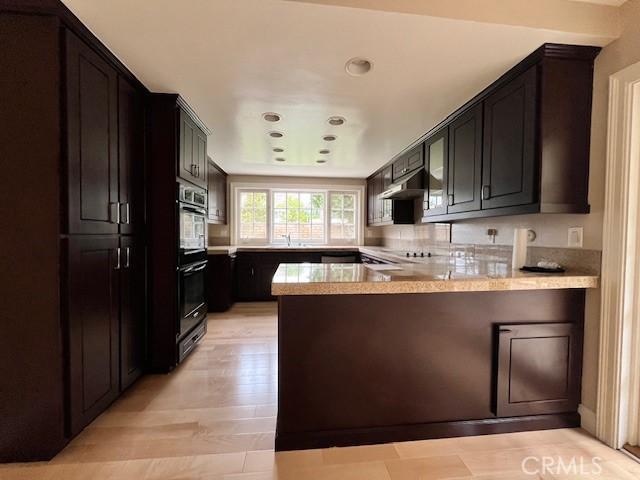 kitchen featuring backsplash, kitchen peninsula, stainless steel double oven, and light wood-type flooring