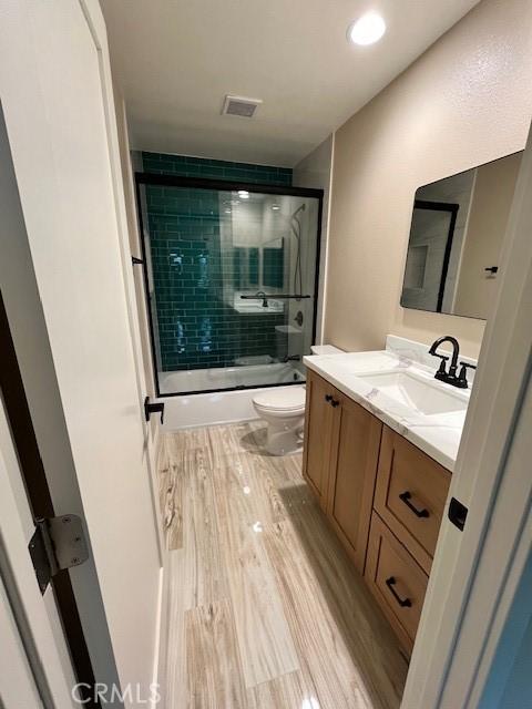 full bathroom featuring combined bath / shower with glass door, hardwood / wood-style floors, vanity, and toilet