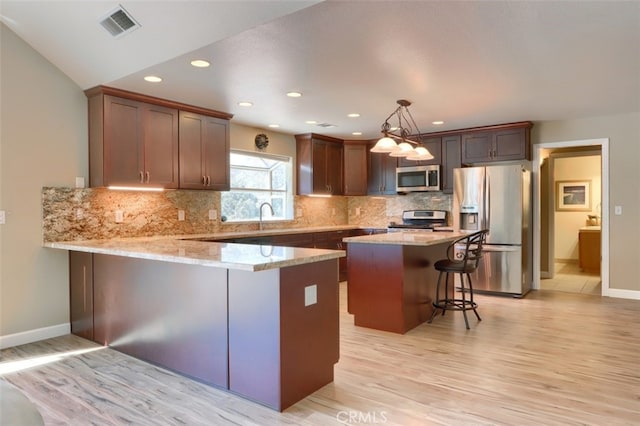 kitchen featuring light hardwood / wood-style flooring, kitchen peninsula, stainless steel appliances, a kitchen bar, and decorative light fixtures