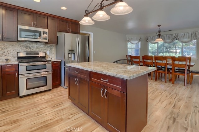 kitchen featuring appliances with stainless steel finishes, backsplash, a center island, light hardwood / wood-style floors, and decorative light fixtures