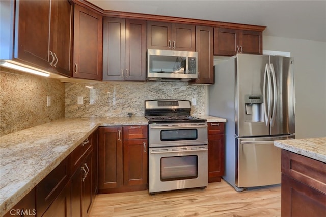 kitchen with light stone counters, stainless steel appliances, decorative backsplash, and light hardwood / wood-style flooring