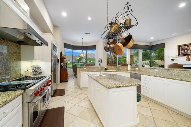 kitchen featuring premium appliances, extractor fan, a kitchen island with sink, and light stone counters