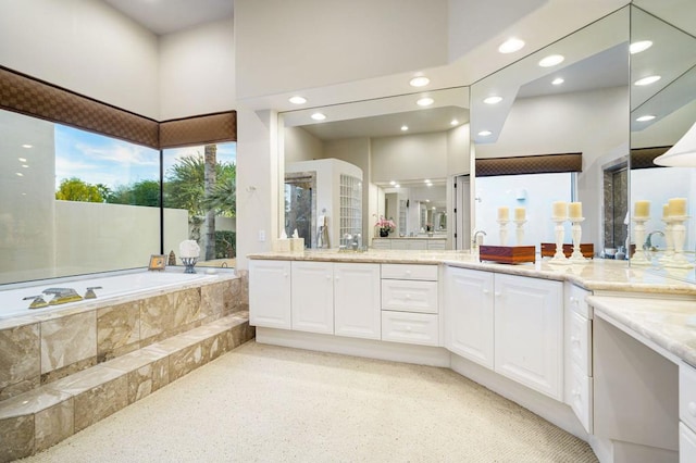 bathroom featuring vanity, a towering ceiling, and tiled tub