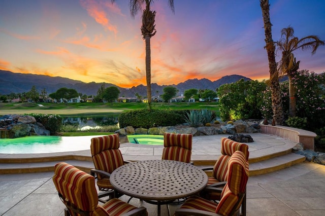 patio terrace at dusk with a water and mountain view and a hot tub