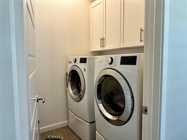 clothes washing area featuring tile patterned floors, cabinet space, baseboards, and washing machine and clothes dryer