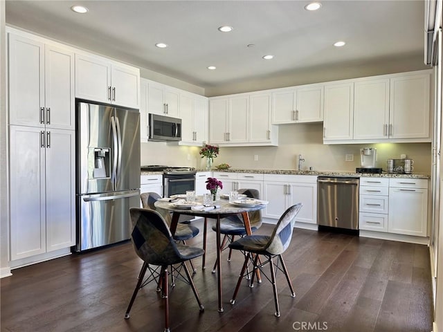 kitchen featuring white cabinetry, appliances with stainless steel finishes, dark wood-type flooring, light stone counters, and sink