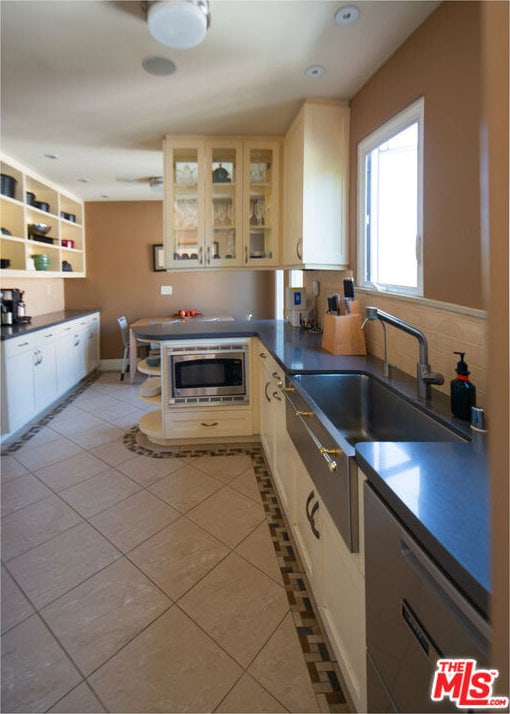 kitchen with stainless steel microwave, white cabinets, sink, light tile patterned floors, and kitchen peninsula