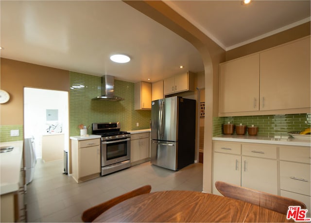 kitchen featuring decorative backsplash, ornamental molding, wall chimney range hood, and appliances with stainless steel finishes