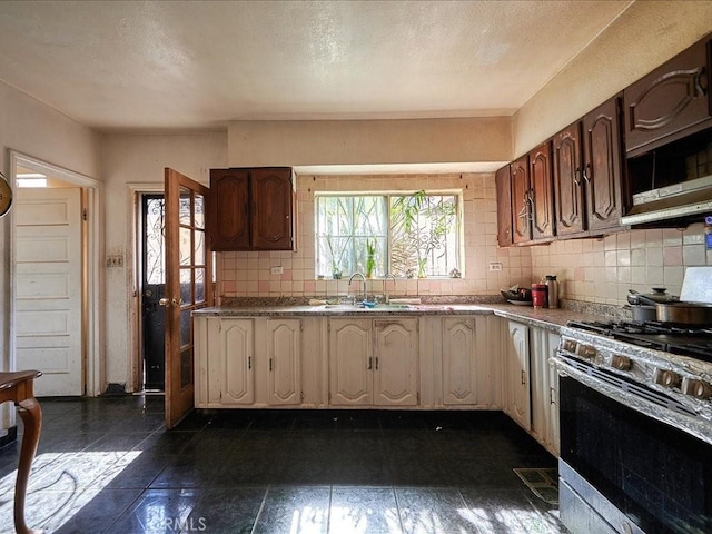 kitchen featuring sink, a textured ceiling, decorative backsplash, dark tile patterned flooring, and stainless steel range with gas stovetop