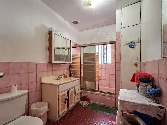 full bathroom featuring toilet, tile patterned flooring, tile walls, and combined bath / shower with glass door