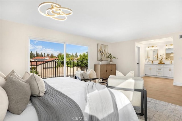 bedroom featuring access to exterior, light hardwood / wood-style flooring, ensuite bath, and a notable chandelier