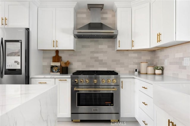 kitchen featuring light stone countertops, appliances with stainless steel finishes, tasteful backsplash, wall chimney range hood, and white cabinetry