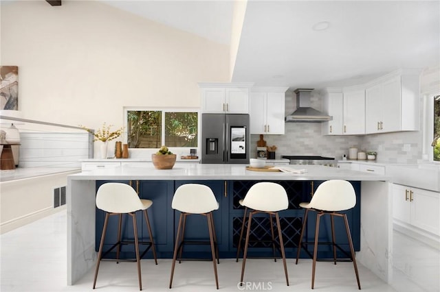 kitchen featuring white cabinets, wall chimney exhaust hood, stainless steel fridge, and a kitchen island