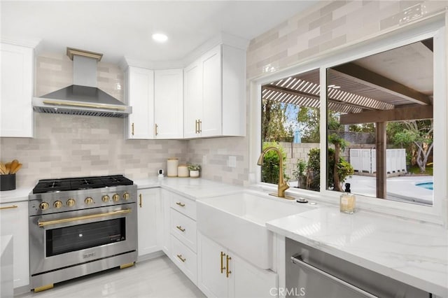 kitchen with wall chimney range hood, light stone counters, decorative backsplash, white cabinets, and appliances with stainless steel finishes