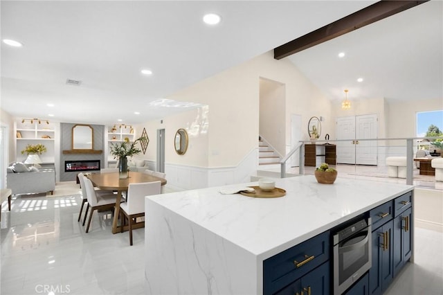 kitchen featuring a large fireplace, a center island, light stone counters, lofted ceiling with beams, and blue cabinets