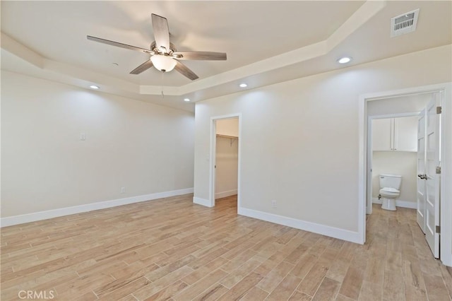 unfurnished room with light hardwood / wood-style floors, a raised ceiling, and ceiling fan