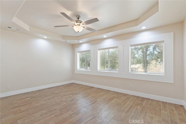 empty room featuring light wood-type flooring, a tray ceiling, and ceiling fan