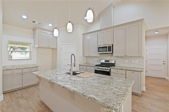 kitchen with hanging light fixtures, stainless steel appliances, light hardwood / wood-style flooring, decorative backsplash, and a center island with sink