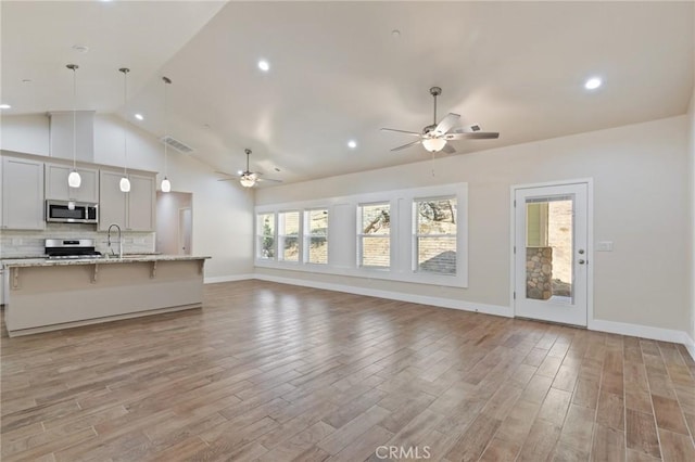 unfurnished living room with hardwood / wood-style flooring, ceiling fan, sink, and high vaulted ceiling