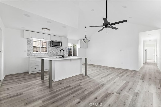 kitchen with a kitchen island with sink, hanging light fixtures, light hardwood / wood-style flooring, white cabinetry, and a breakfast bar area