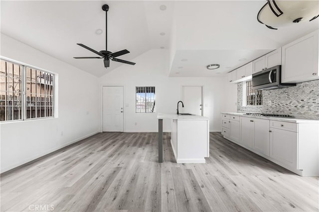 kitchen featuring appliances with stainless steel finishes, a center island with sink, light hardwood / wood-style flooring, white cabinetry, and lofted ceiling