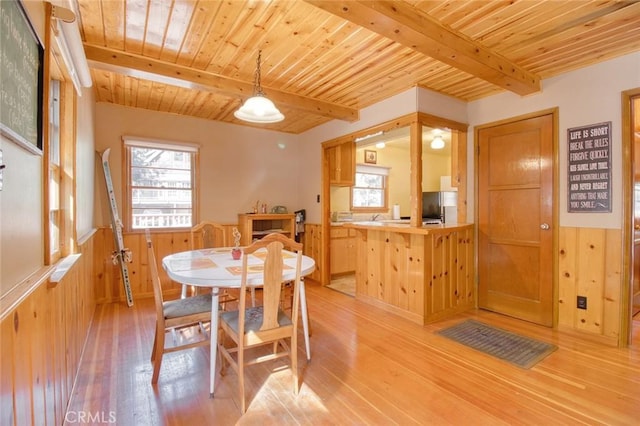 dining room featuring beamed ceiling, plenty of natural light, light wood-type flooring, and wooden walls