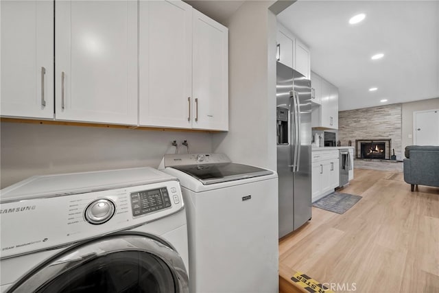 clothes washing area with washing machine and dryer, cabinets, a fireplace, and light wood-type flooring