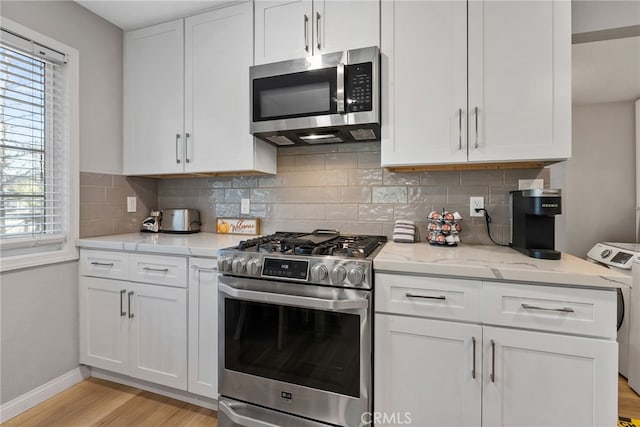 kitchen with white cabinetry, appliances with stainless steel finishes, light wood-type flooring, and decorative backsplash